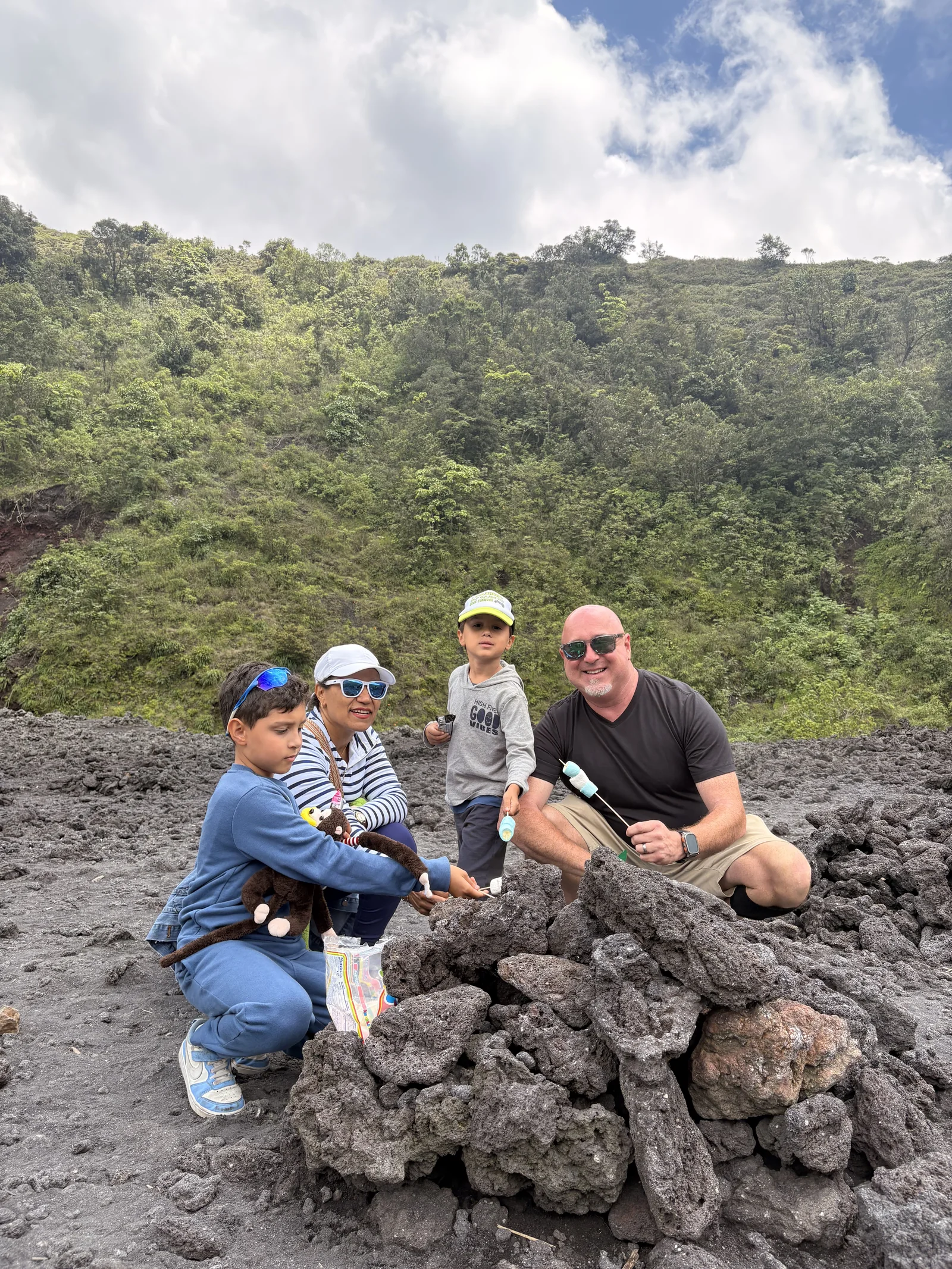 Andrew McGilly and his family roasting marshmallows over a pile of warm lava rock on the Pacaya lava field, with a green slope behind